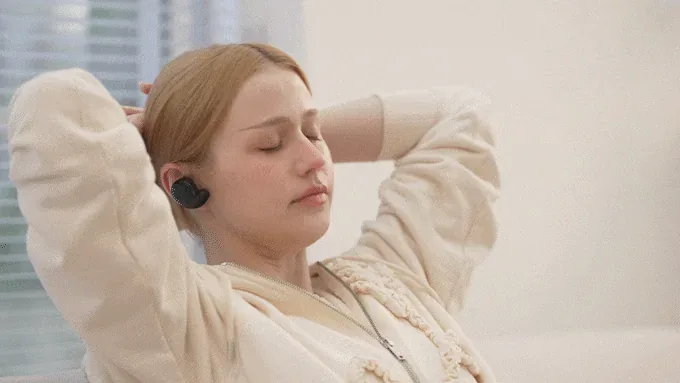 A woman reclining with her eyes closed, relaxing with a BeCozU device in her left ear